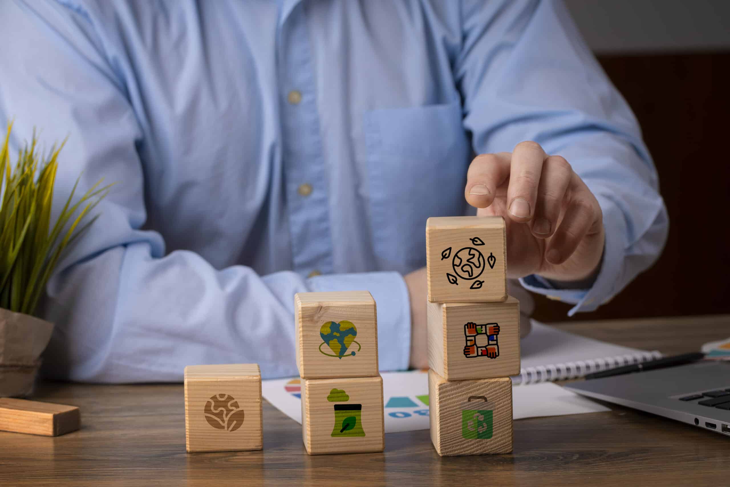 Homem organizando blocos de madeira com ícones de sustentabilidade, governança corporativa e responsabilidade social em um escritório.